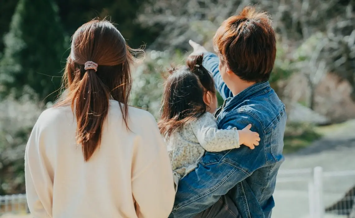 「屋外で自然を見ながら家族で過ごす様子。父親が子どもを抱き、遠くを指差している。母親も寄り添っている。