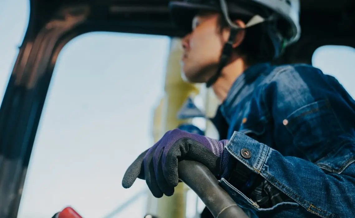 重機を操作する作業員。ヘルメットと手袋を着用し、真剣な表情で作業している。