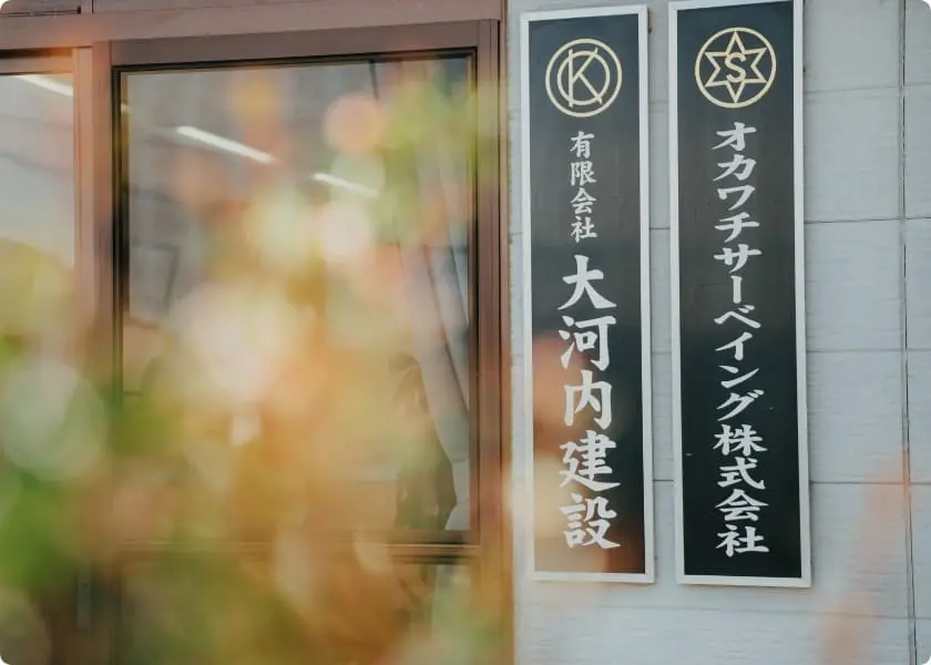 建物の外壁に掲げられた会社の看板。左に『有限会社 大河内建設』、右に『オカワチサーベイング株式会社』と記されている。
