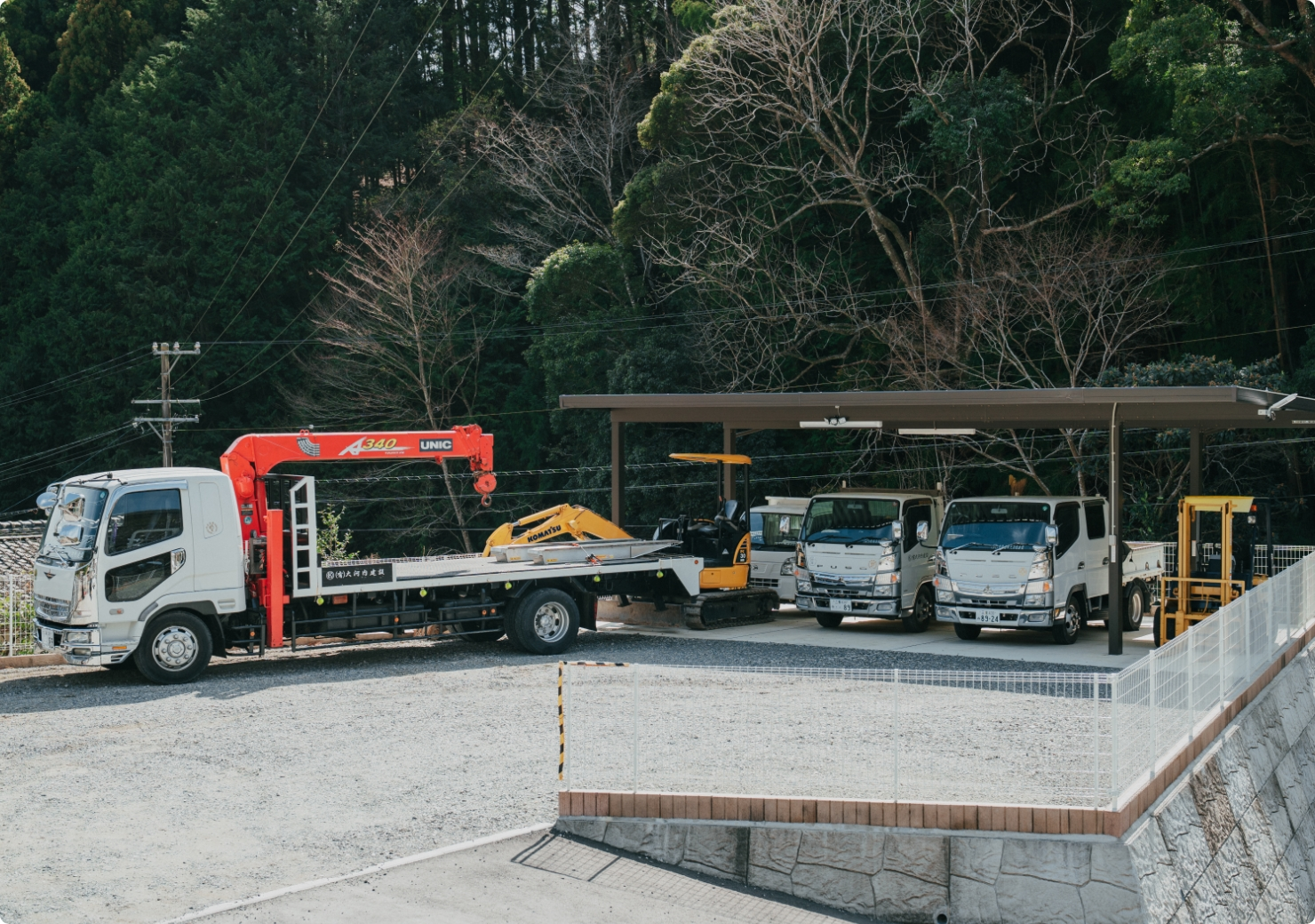 白い作業車がいくつか並んだカーポートと砂利の駐車場。